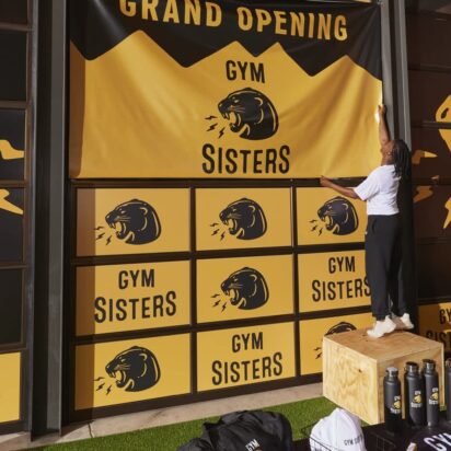 Small business owner hanging a branded Gym Sisters banner on her gym’s storefront window.