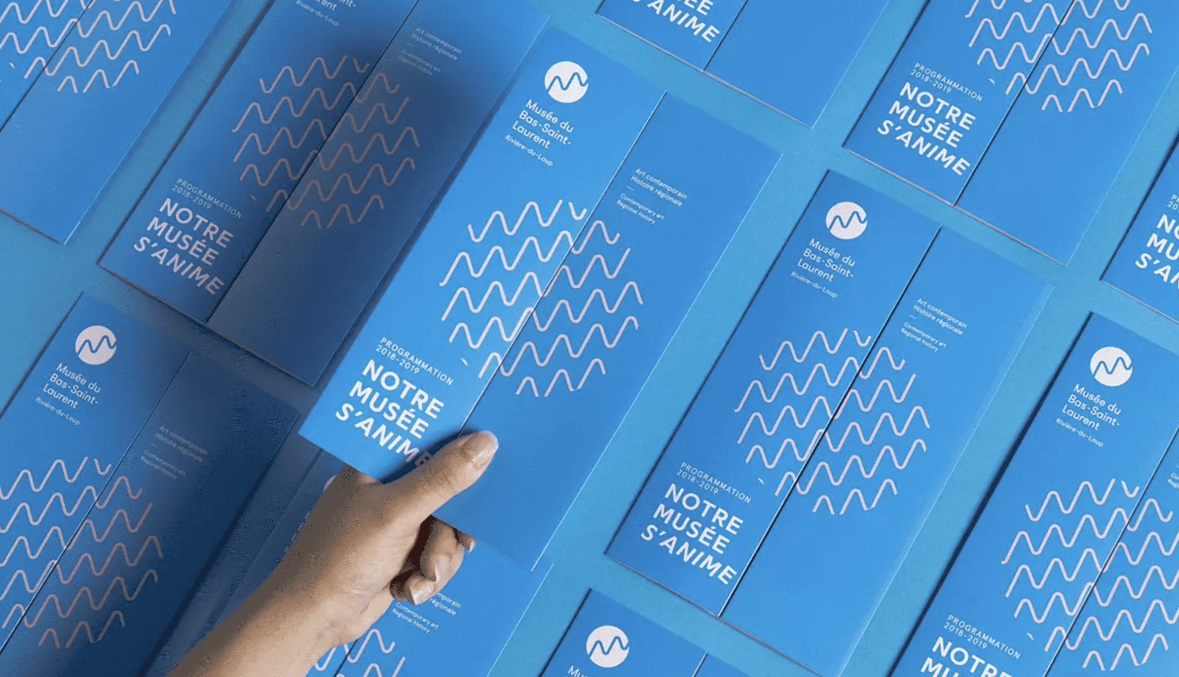 A hand picking up one of a number of Mus&eacute;e du Bas-Saint-Laurent brochures